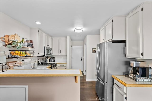 kitchen with light countertops, appliances with stainless steel finishes, dark wood-type flooring, white cabinets, and a peninsula