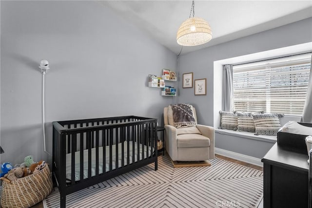 bedroom with vaulted ceiling, a crib, baseboards, and wood finished floors