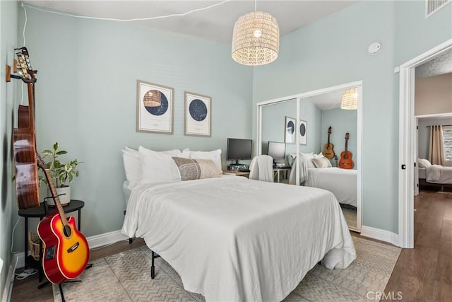 bedroom with baseboards, a closet, visible vents, and wood finished floors