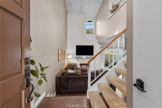 foyer featuring stairs, a high ceiling, a fireplace, and wood finished floors