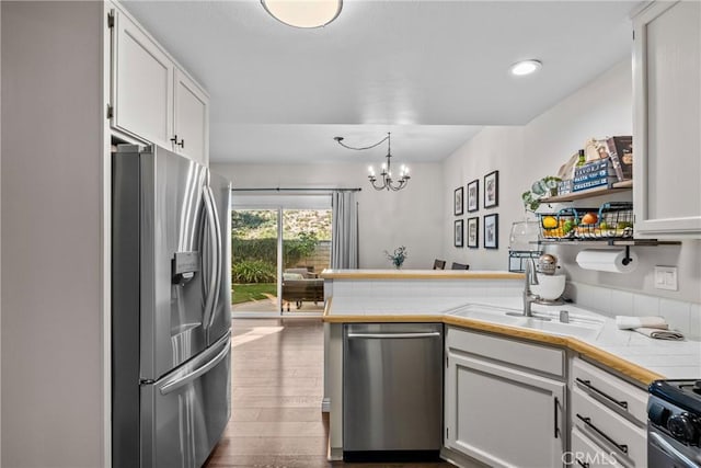 kitchen featuring tile countertops, stainless steel appliances, a peninsula, white cabinetry, and an inviting chandelier