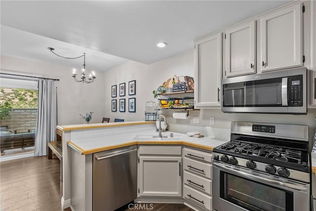 kitchen with tile counters, white cabinets, appliances with stainless steel finishes, a peninsula, and a sink