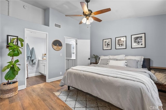 bedroom featuring visible vents, ensuite bathroom, wood finished floors, high vaulted ceiling, and baseboards