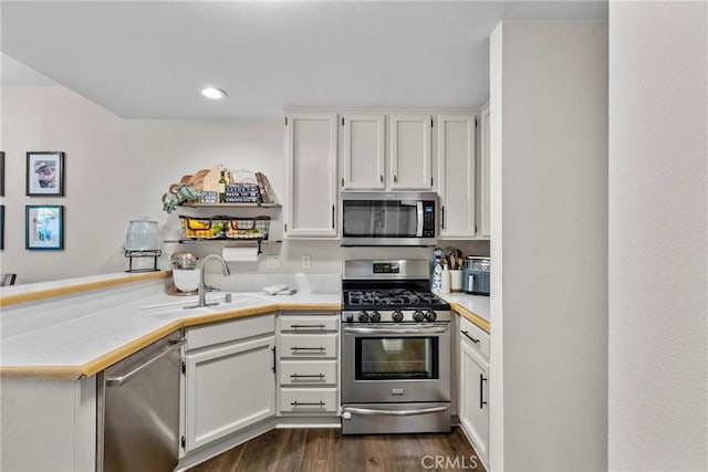 kitchen featuring a peninsula, a sink, white cabinets, appliances with stainless steel finishes, and dark wood-style floors