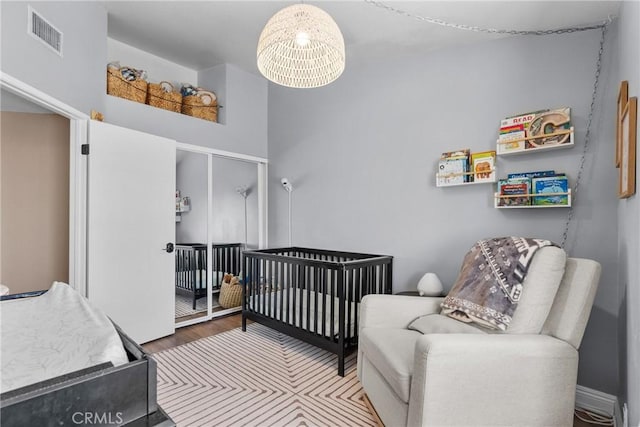 bedroom featuring a nursery area, wood finished floors, and visible vents