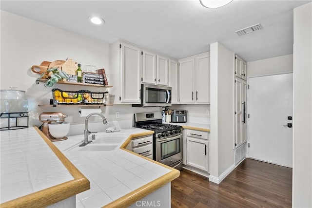 kitchen with a sink, visible vents, appliances with stainless steel finishes, tile counters, and dark wood-style floors