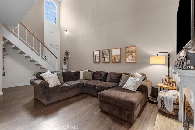 living room featuring a towering ceiling, stairs, baseboards, and wood finished floors