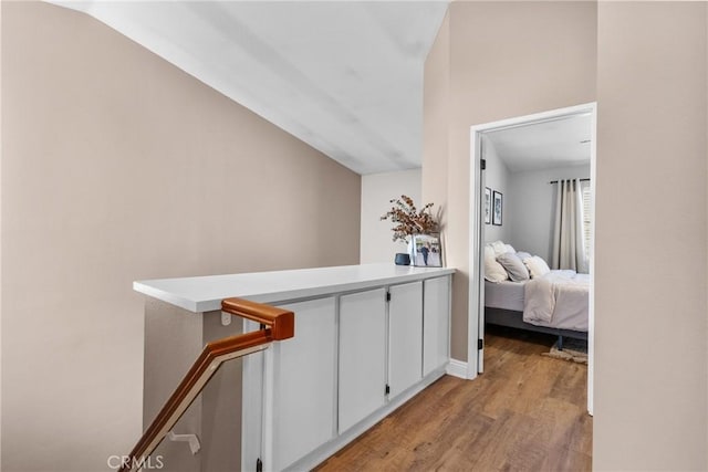 hall with baseboards, vaulted ceiling, light wood-style flooring, and an upstairs landing