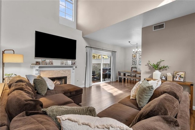 living room featuring a fireplace, visible vents, a high ceiling, an inviting chandelier, and wood finished floors