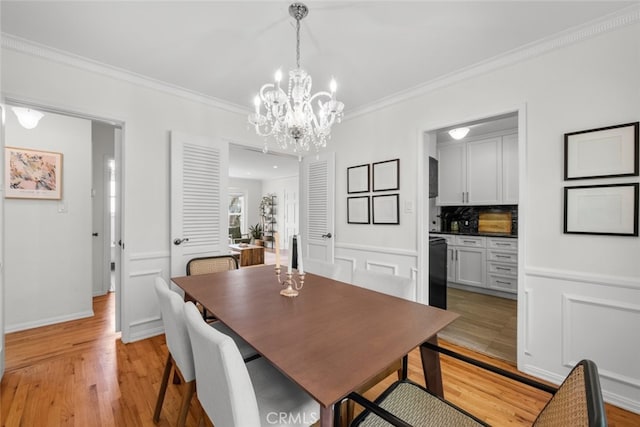 dining room featuring a wainscoted wall, ornamental molding, light wood-style flooring, and a decorative wall