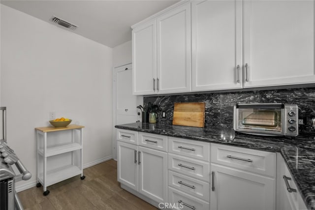 kitchen featuring wood finished floors, white cabinetry, visible vents, decorative backsplash, and dark stone countertops