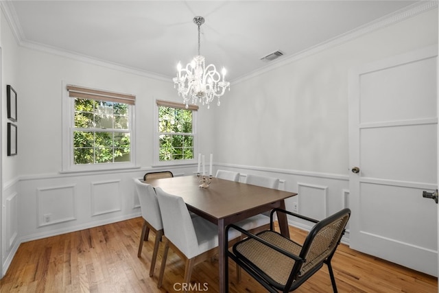 dining space featuring visible vents, crown molding, a decorative wall, and light wood finished floors