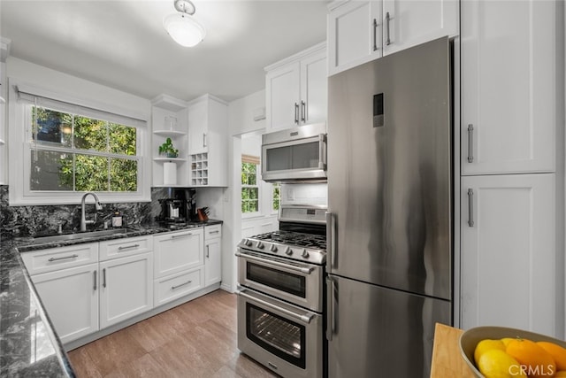 kitchen with light wood finished floors, decorative backsplash, appliances with stainless steel finishes, white cabinetry, and a sink