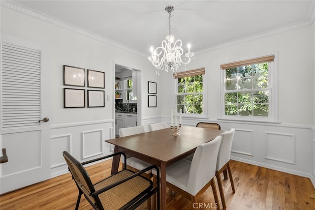 dining room featuring a wainscoted wall, ornamental molding, light wood-type flooring, a decorative wall, and a notable chandelier