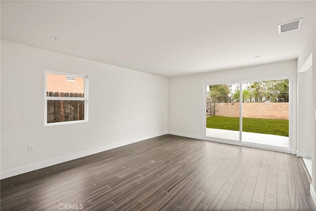 spare room with dark wood-style floors, visible vents, and baseboards