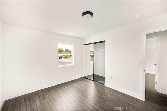 unfurnished bedroom with dark wood-style floors, a closet, and baseboards