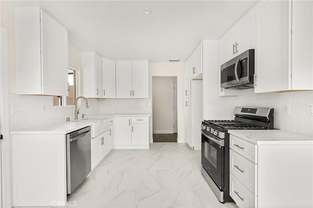 kitchen featuring stainless steel appliances, a sink, white cabinetry, marble finish floor, and decorative backsplash