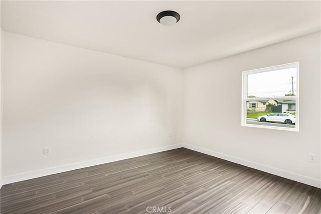 spare room featuring baseboards and dark wood-style flooring