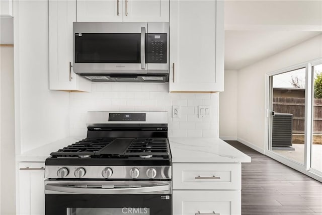 kitchen with white cabinets, appliances with stainless steel finishes, light stone counters, wood finished floors, and backsplash