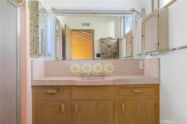 bathroom with a shower with shower door, visible vents, vanity, and decorative backsplash