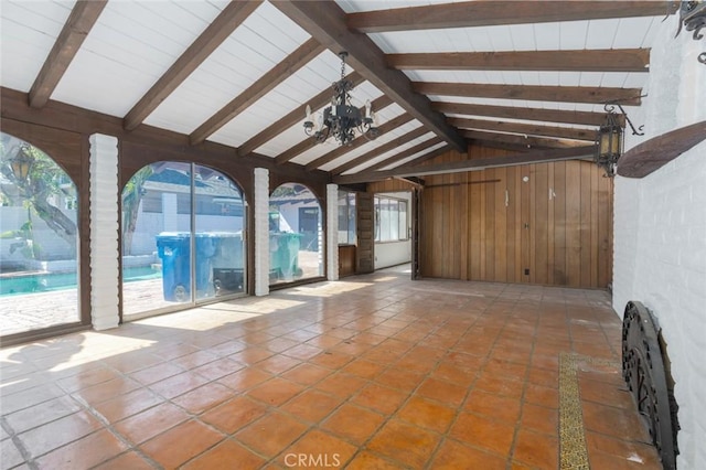 unfurnished living room featuring vaulted ceiling with beams, wood walls, tile patterned flooring, and a notable chandelier