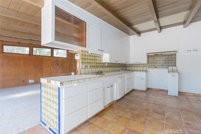 kitchen with wooden walls, white cabinets, tile countertops, beamed ceiling, and backsplash