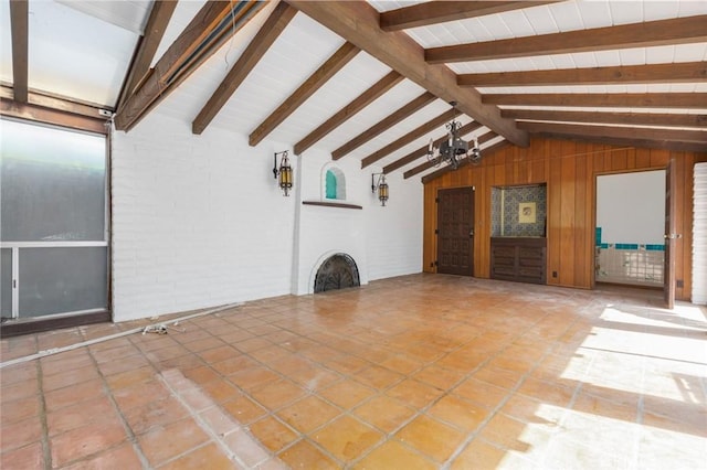 unfurnished living room featuring tile patterned flooring, vaulted ceiling with beams, and brick wall