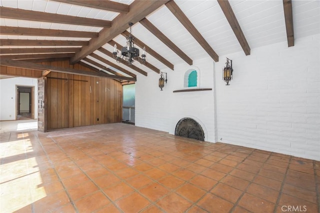 unfurnished living room with a brick fireplace, lofted ceiling with beams, brick wall, and light tile patterned floors