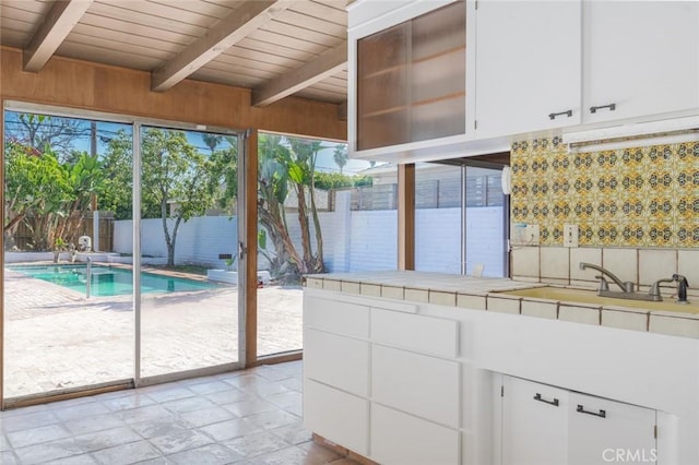 kitchen with wooden ceiling, tile counters, white cabinetry, and beam ceiling