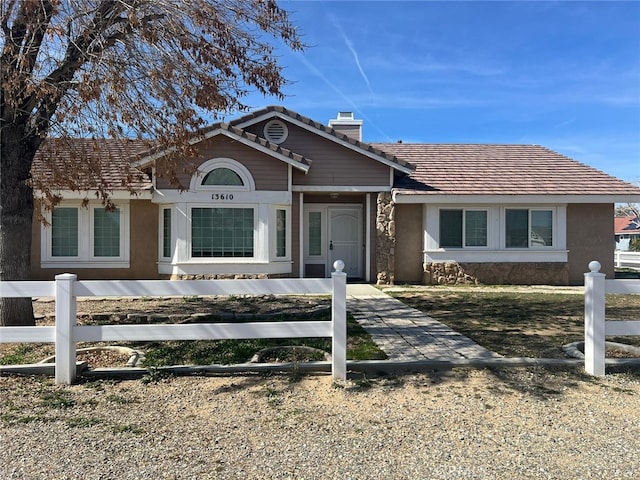 view of front facade featuring a tile roof, a fenced front yard, a chimney, and stucco siding