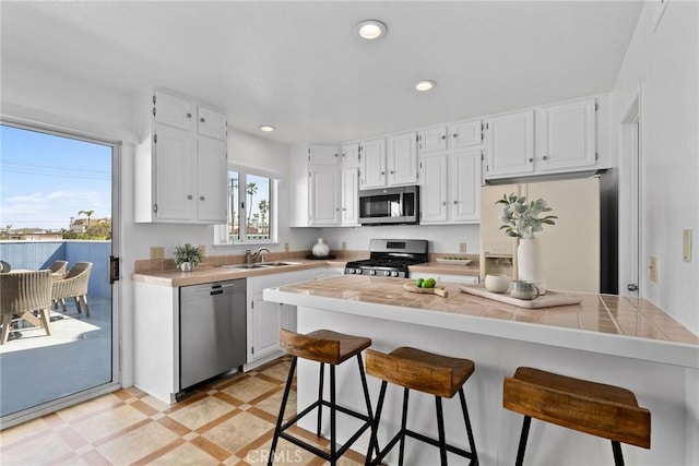 26B Surfside Ave, Surfside, CA 90743 - kitchen with appliances with stainless steel finishes, tile counters, white cabinetry, a breakfast bar area, and recessed lighting