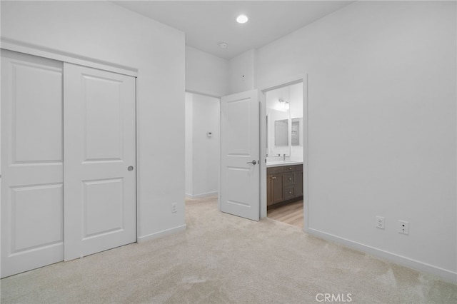 unfurnished bedroom with a closet, light carpet, a sink, and baseboards