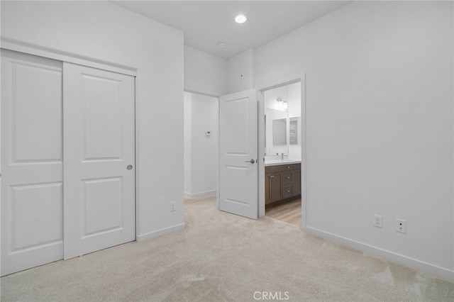 unfurnished bedroom featuring baseboards, light carpet, a closet, and connected bathroom