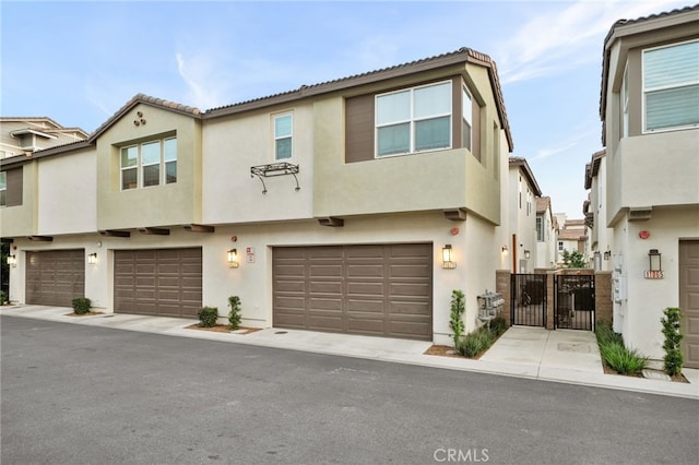 townhome / multi-family property with a garage, a tile roof, a gate, and stucco siding