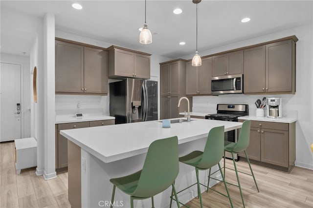 kitchen featuring stainless steel appliances, light countertops, a center island with sink, and light wood-style flooring