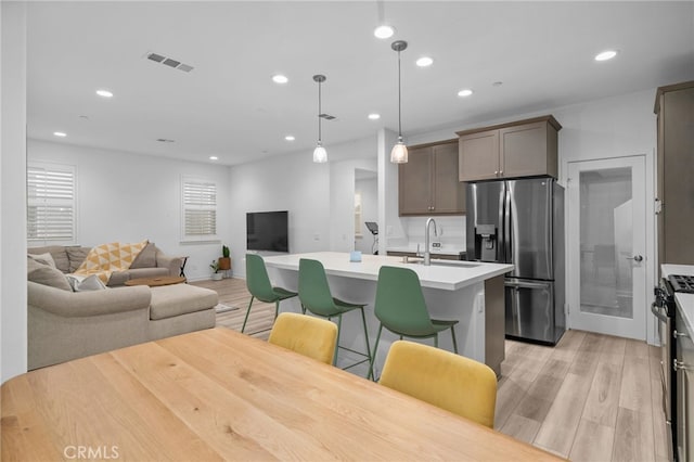 kitchen with an island with sink, light wood finished floors, visible vents, and stainless steel appliances