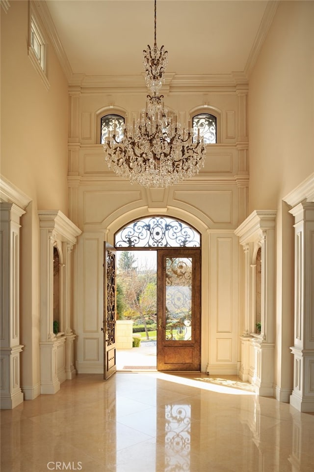 interior space with decorative columns, a high ceiling, ornamental molding, and a notable chandelier