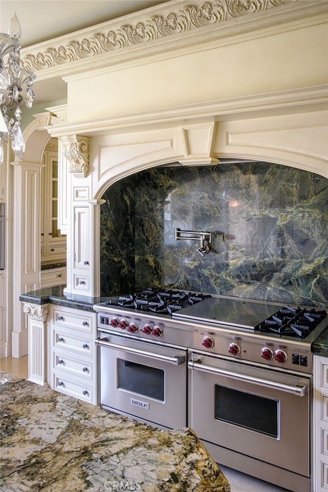 kitchen featuring cream cabinetry, double oven range, backsplash, and dark stone countertops