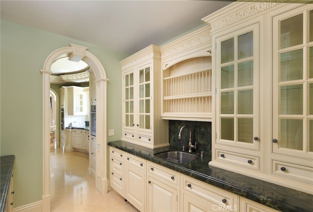 kitchen with cream cabinets, wall oven, a sink, decorative backsplash, and glass insert cabinets