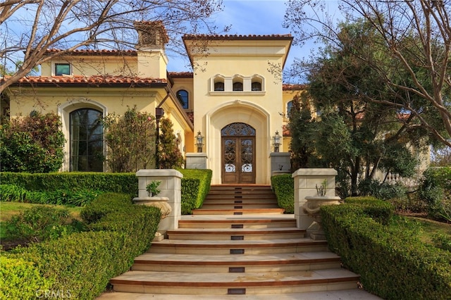 entrance to property with french doors, a tile roof, a chimney, and stucco siding