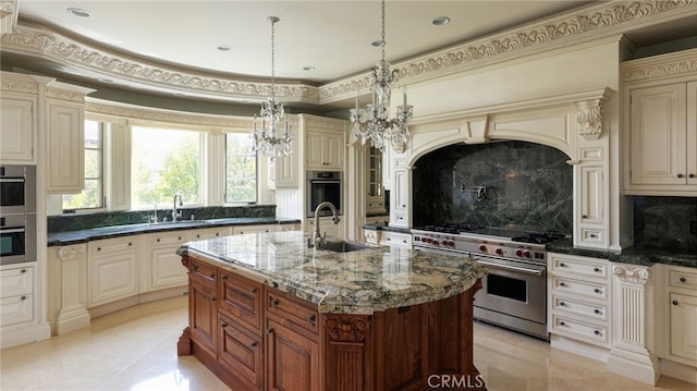 kitchen with stainless steel appliances, cream cabinetry, dark stone countertops, and a sink