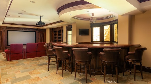 bar with a tray ceiling, stone tile floors, a community bar, ornamental molding, and baseboards