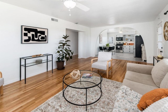 living area with arched walkways, visible vents, ceiling fan, and wood finished floors