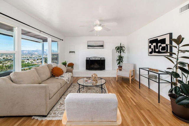 living room with a fireplace, visible vents, light wood-style flooring, ceiling fan, and baseboards