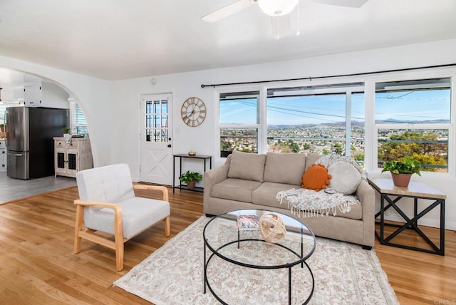 living room with light wood-type flooring, arched walkways, ceiling fan, and baseboards