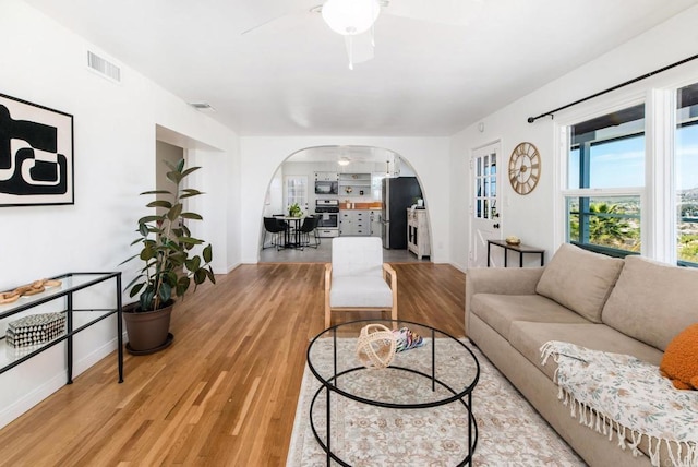 living area featuring arched walkways, wood finished floors, visible vents, baseboards, and a ceiling fan