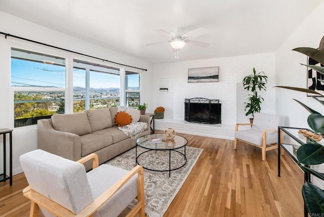 living area with a brick fireplace, ceiling fan, and wood finished floors