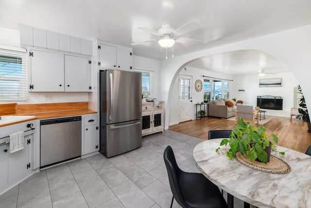 kitchen featuring white cabinetry, stainless steel appliances, arched walkways, a ceiling fan, and a fireplace