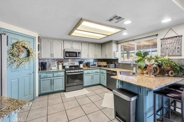 kitchen with backsplash, appliances with stainless steel finishes, a sink, light stone countertops, and a peninsula