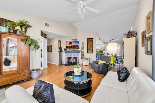 living room with visible vents, a tile fireplace, ceiling fan, wood finished floors, and vaulted ceiling